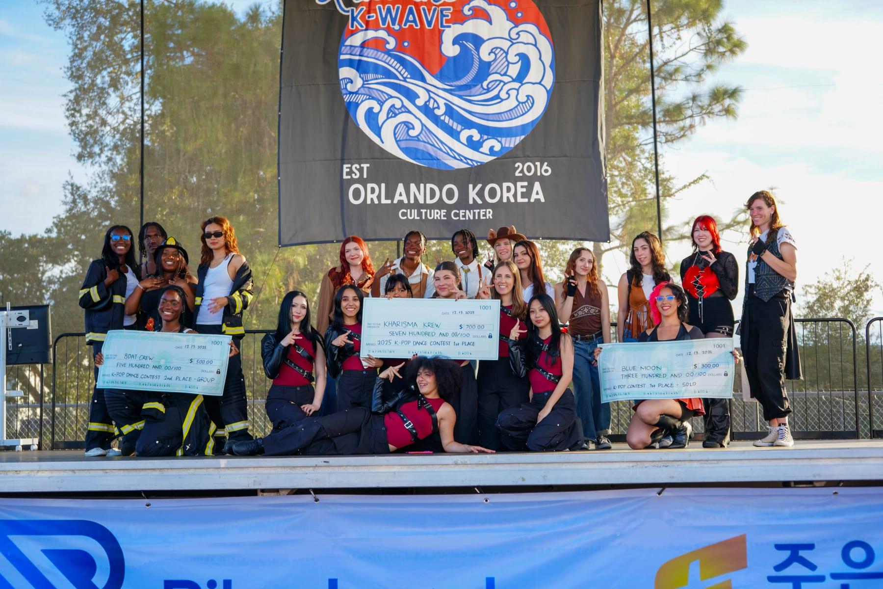 The 2025 K-Pop Dance Contest winners on stage with their prize checks under the Ride the K-Wave banner